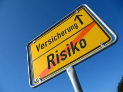Das Bild zeigt ein gelbes Ortsschild mit zwei Aufschriften "Versicherung und Risiko" und verdeutlicht das Risiko bei Abschluss einer Reisekrankenversicherung