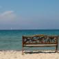 Das Bild zeigt eine Bank aus Holz vor dem Strand und dem Meer. Das Bild steht für Urlaub, Urlaubsgeld und Urlaubsabgeltung 